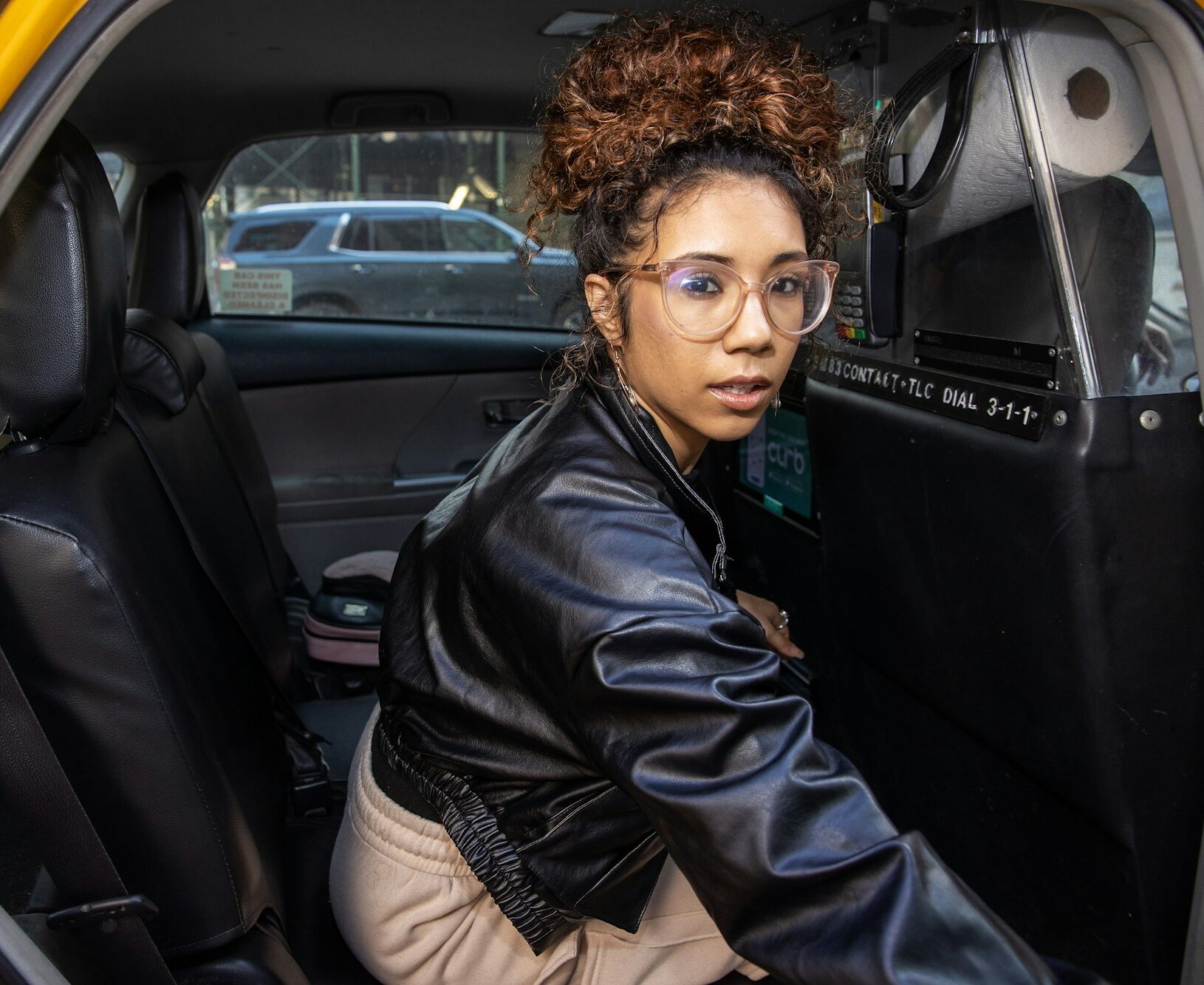 Young mixed race woman wearing black leather jacket in yellow taxi cab for city transportation